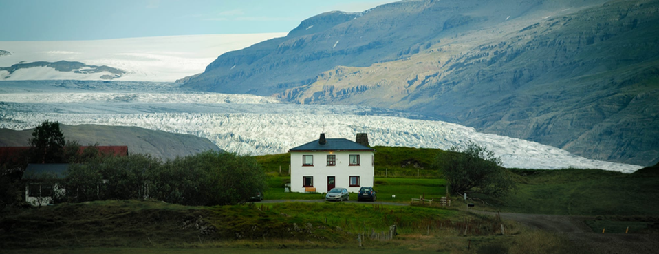 Fotografi av ett bostadshus framför en glaciär och ett bergigt landskap. 