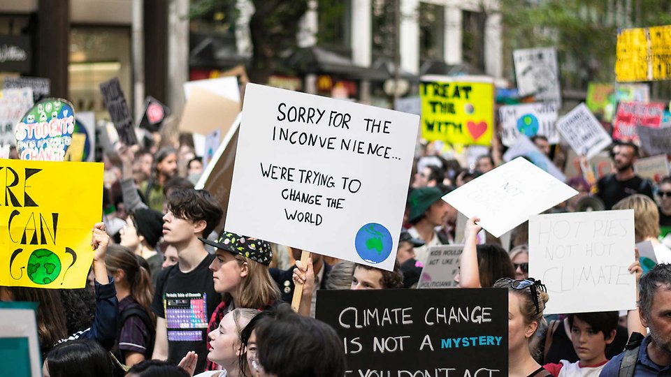Samling med människor som håller upp plakat med budskap om att rädda klimatet.